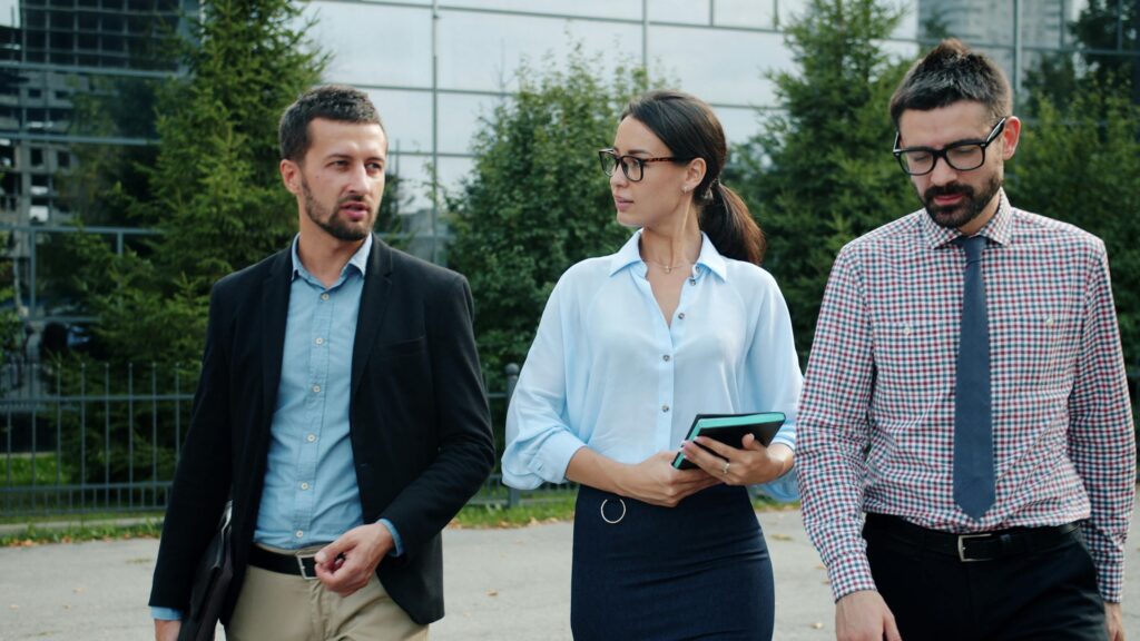 Για την Επιχείρηση Three business professionals walking and discussing ideas outdoors in a modern urban setting.