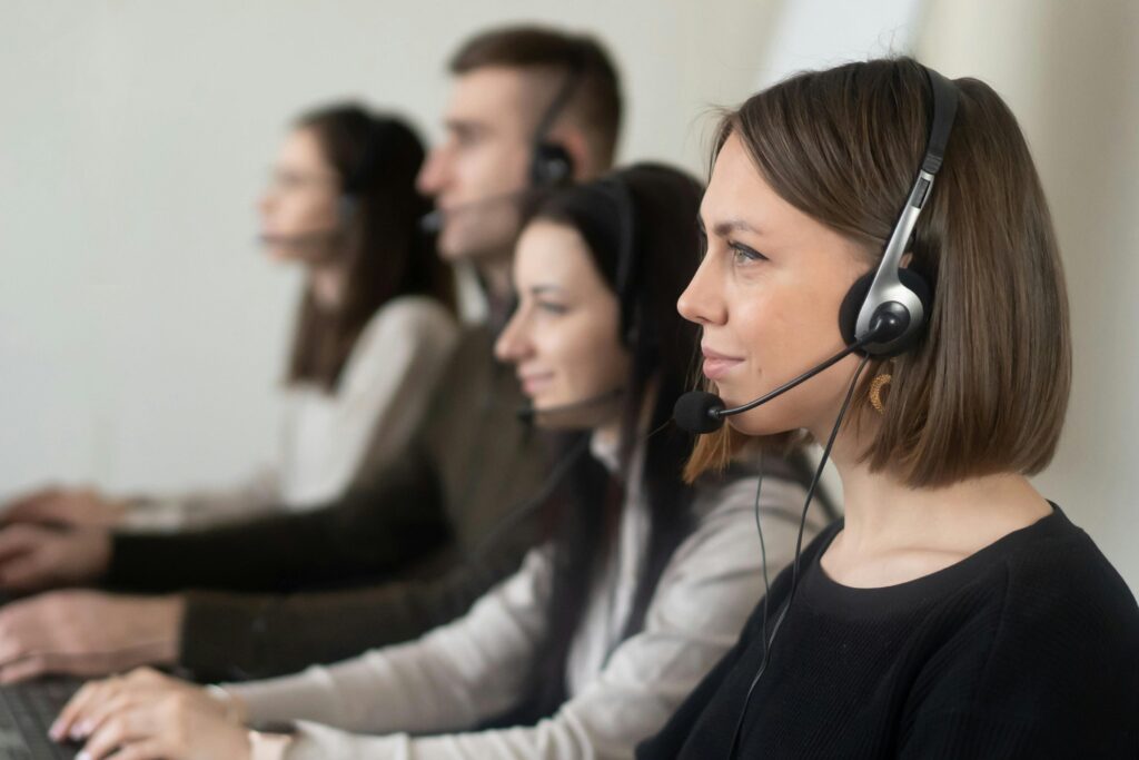 pexels photo 7035859 7035859 Side view of young coworkers in casual clothes sitting in light workplace with headphones with microphone while surfing on laptop