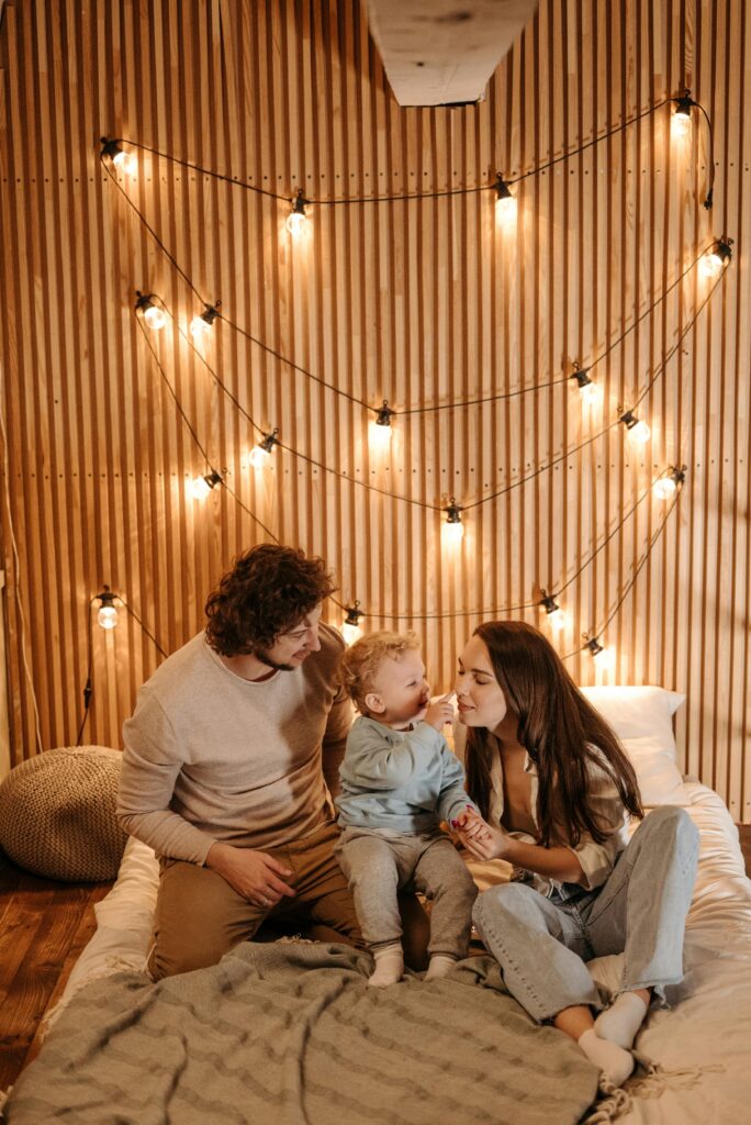 Family bonding in a cozy, warmly lit room with string lights on a wooden wall backdrop.